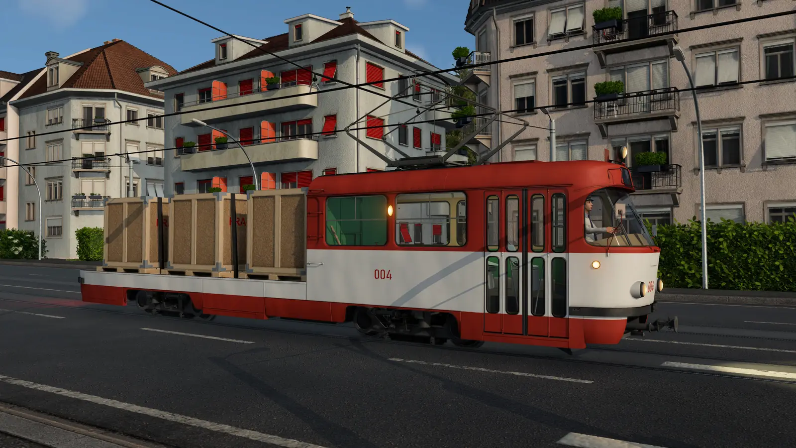 A red and white electric cargo tram in Transport Fever 3 carrying three wooden crates on its flat bed, under overhead wires on a street of apartment houses