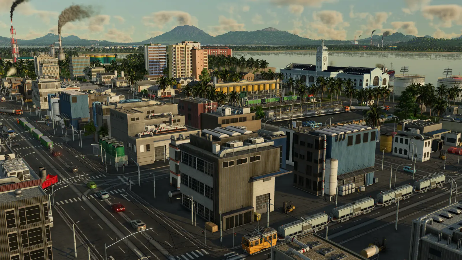 A Transport Fever 3 harbor town in the tropics: factories with smoking chimneys, apartment blocks, freight trains and a yellow tram in the streets, and a white building with a clock tower by the water, with mountains behind