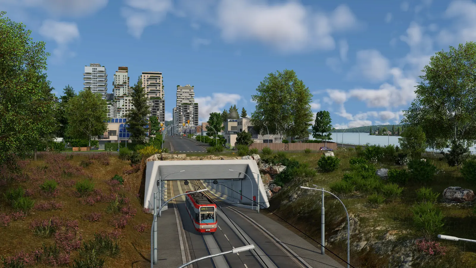 A red and white Line 1 tram on a light railway at the mouth of a tunnel under a street in Transport Fever 3, with high-rise buildings and a lake behind
