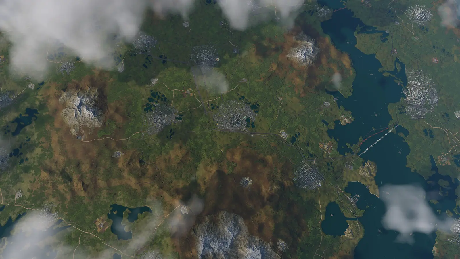 A whole Transport Fever 3 map seen from high above, with towns, rail lines, lakes and snow-capped mountains under scattered clouds